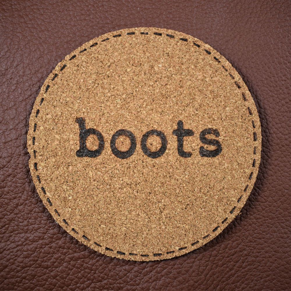 A circle of brown cork  material with "boots" burned into it on top of a piece of leather