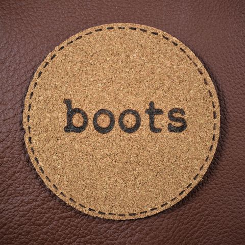 A circle of brown cork  material with "boots" burned into it on top of a piece of leather